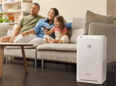 Family sitting on a couch with an air purifier in the foreground